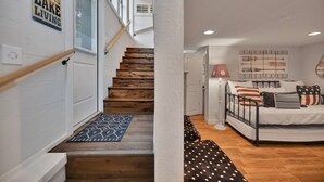 Una escala de fusta que porta a una habitació amb llit, una tauleta de nit i una làmpada penjada a la paret.