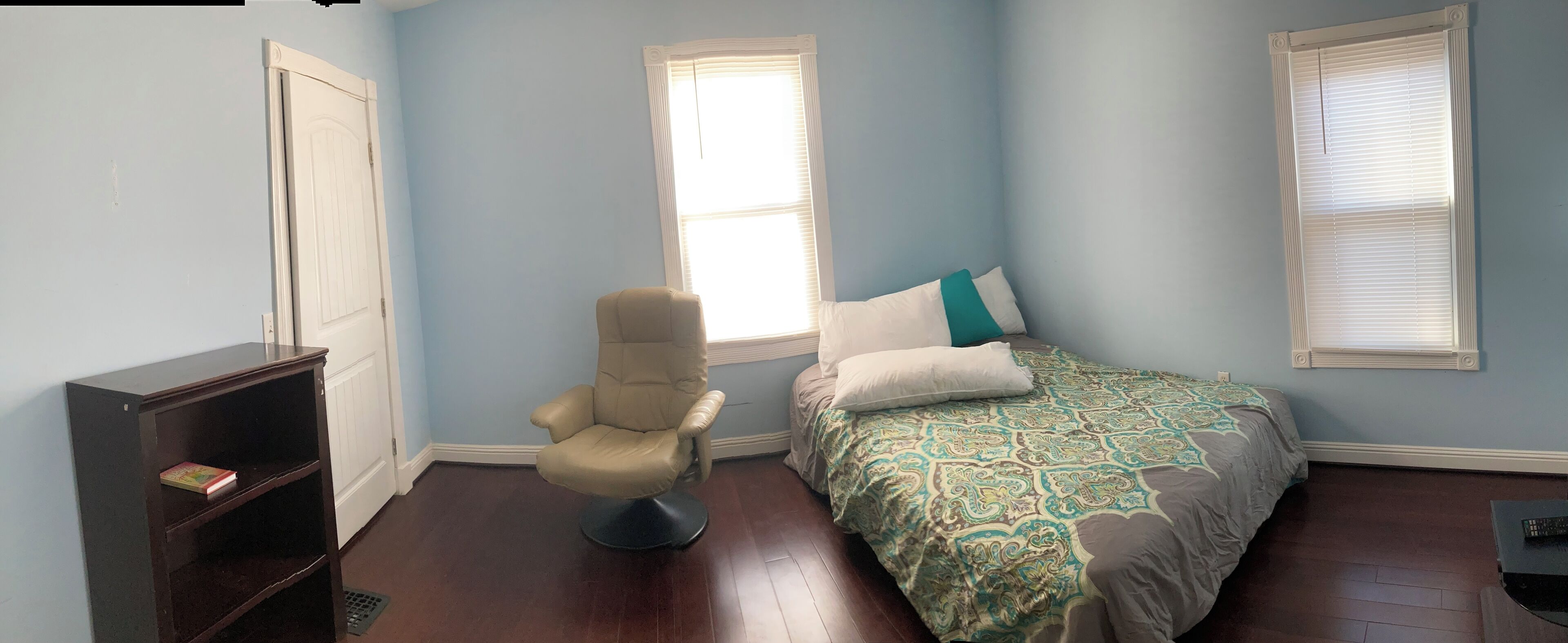 Un dormitorio con cama, una silla, una estantería y dos ventanas.