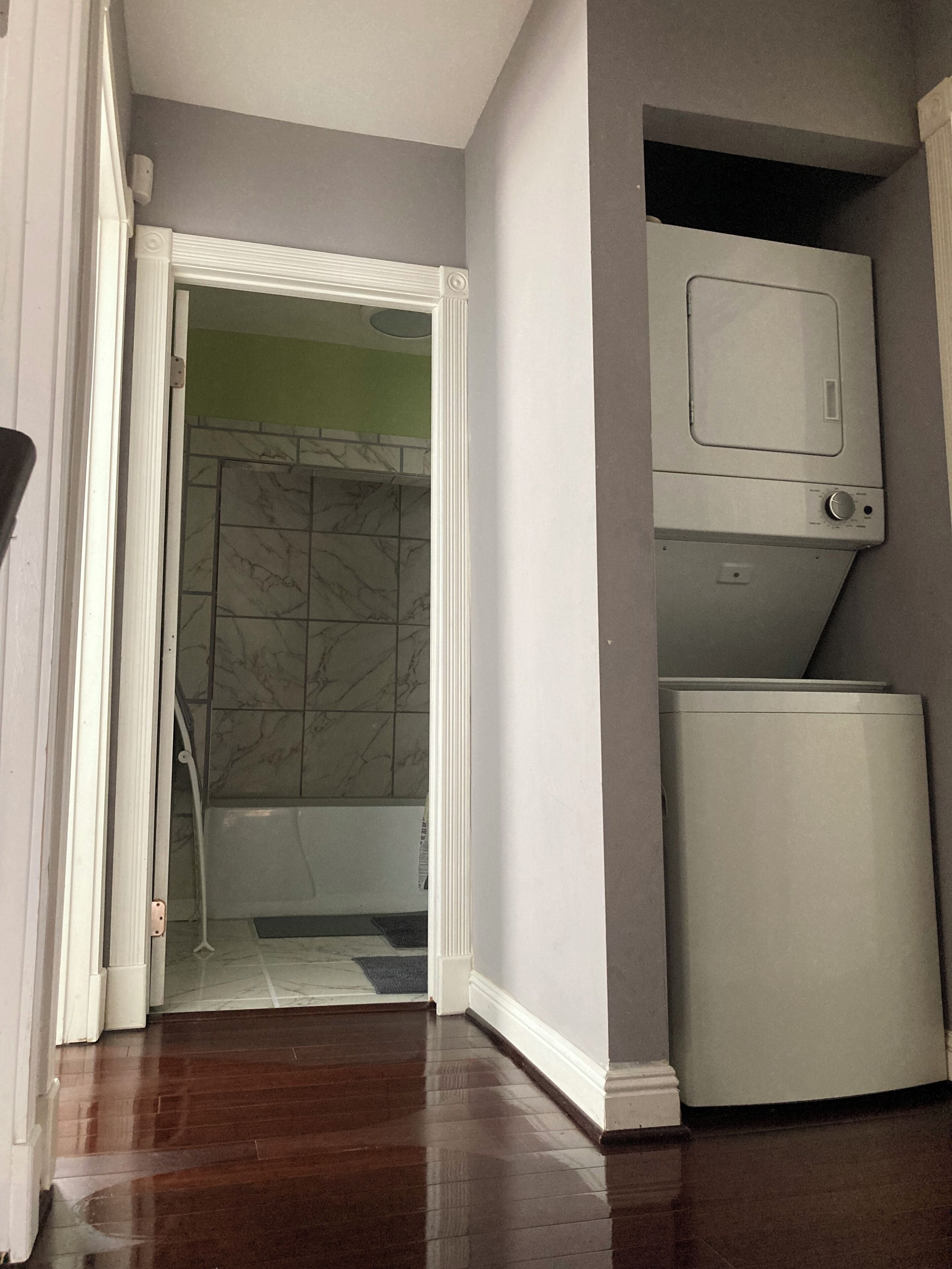 Ein Zimmer mit Holzboden, einer weißen Tür zu einem Badezimmer mit Dusche und einem weißen Gerät an der Wand.