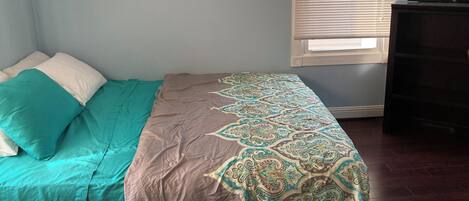 A bedroom with a bed, a window with blinds, and a dark dresser.