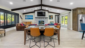 A spacious dining area with a high ceiling, a fireplace, and a large window offering a view of greenery. - Inspiration House-One Acre Pool Home in the Heart of Pinellas!  (Pinellas Park)