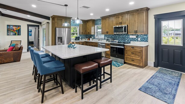 A modern kitchen with a central island, bar stools, wooden cabinets, and a large window. - Inspiration House-One Acre Pool Home in the Heart of Pinellas!  (Pinellas Park)