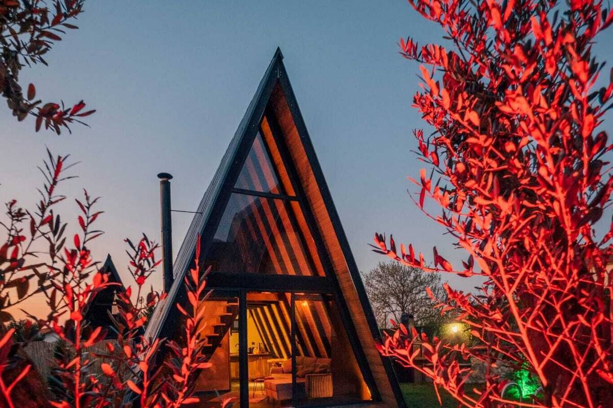 Un edificio moderno triangular con piscina delantera, rodeado de follaje rojo.