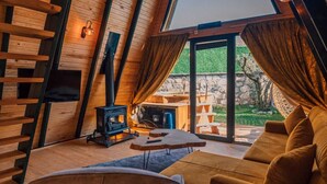 A cozy attic room with a wooden interior, a fireplace, a sofa, and a large window offering a view of the outdoors. - KARMATTE BUNGALOW  (Kartepe)