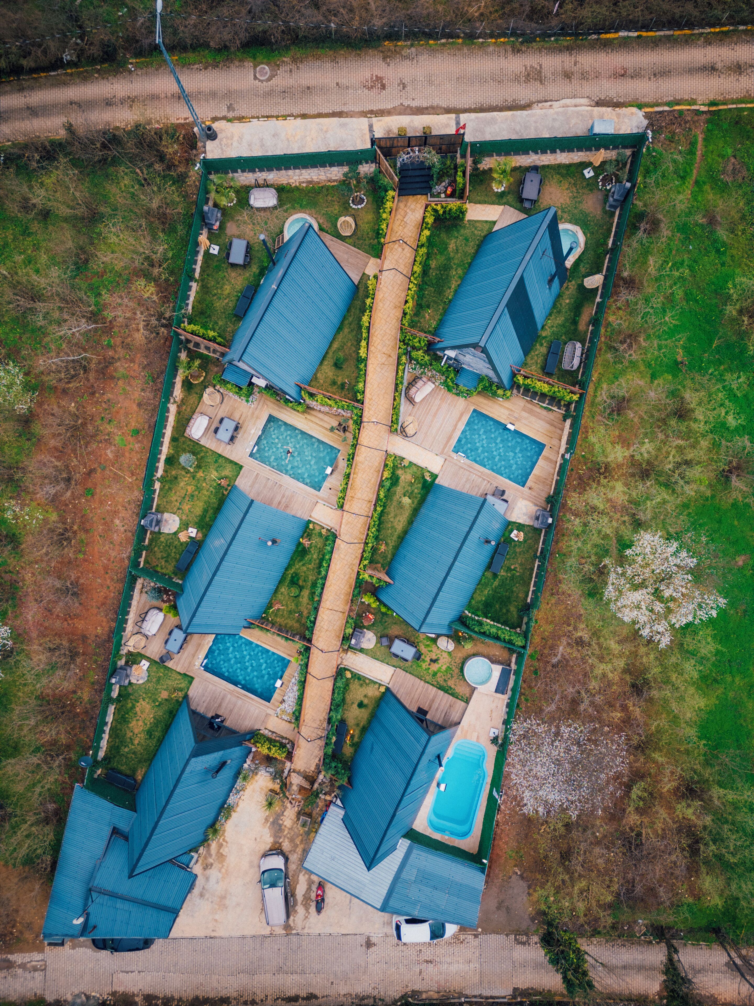 An aerial view of a residential complex with multiple blue-roofed houses, a central walkway, and a swimming pool area.