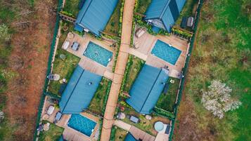 An aerial view of a residential complex with multiple blue-roofed houses, a central walkway, and a swimming pool area.