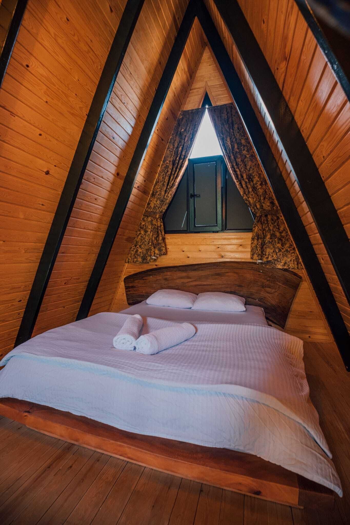 A cozy, wooden-paneled attic bedroom with a bed, pillows, and a window with curtains.