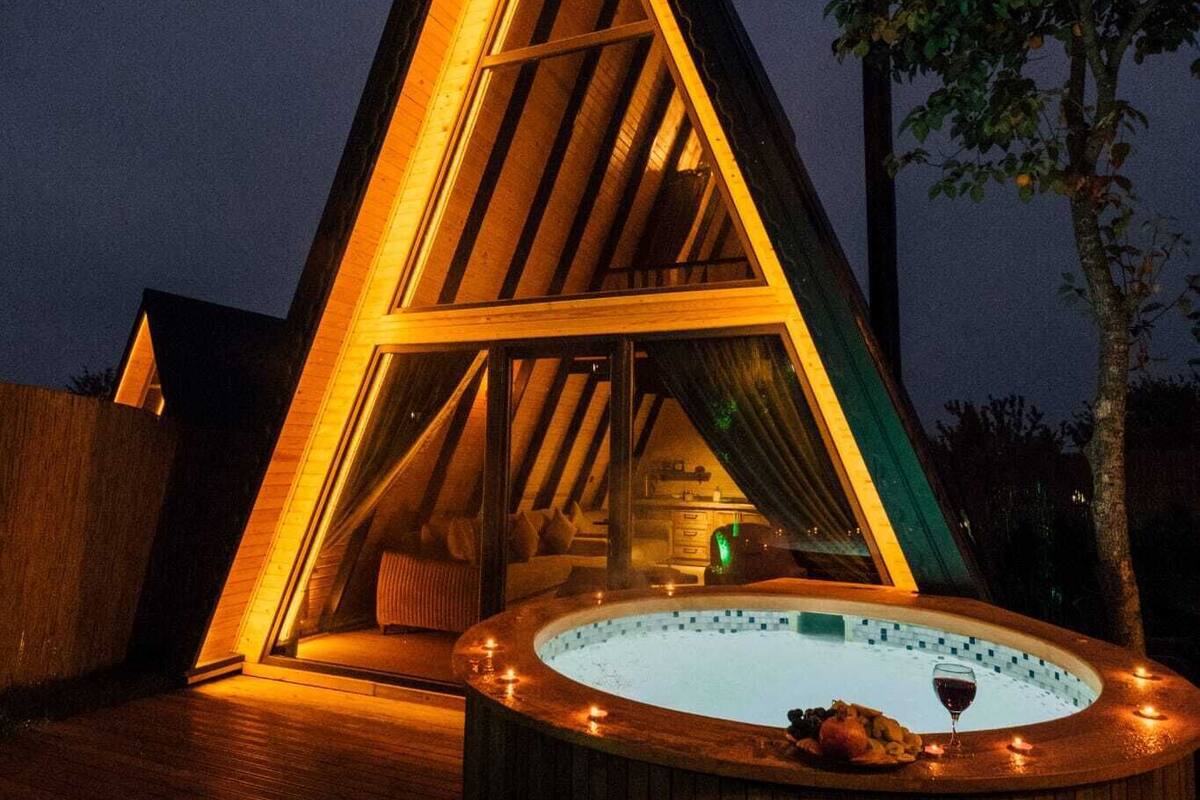 Una estructura de madera triangular con un jacuzzi en el centro, rodeado por una terraza de madera.