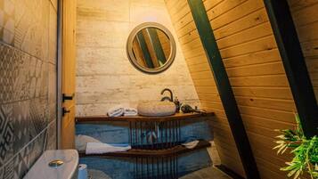 A small, cozy bathroom with a wooden ceiling, a round mirror, a sink, and a toilet.