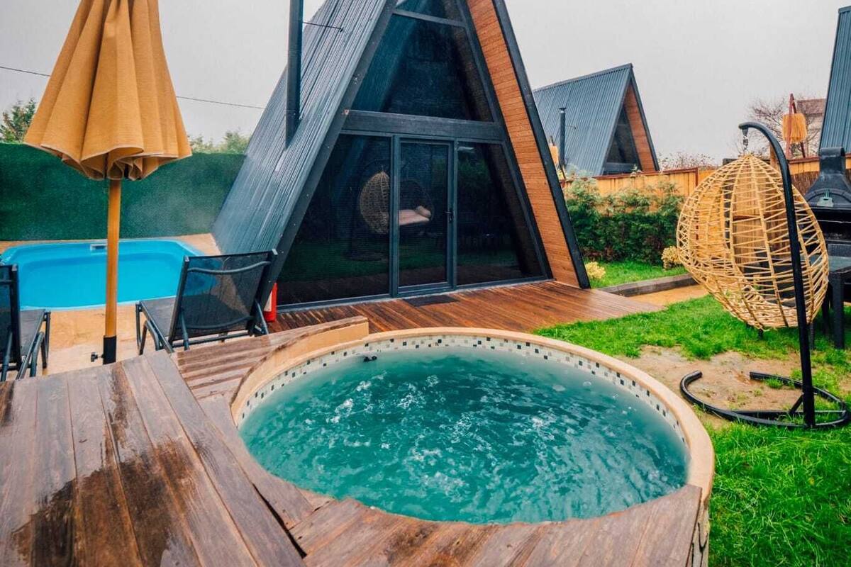 Un edificio moderno de techo triangular con terraza de madera y un jacuzzi al frente.