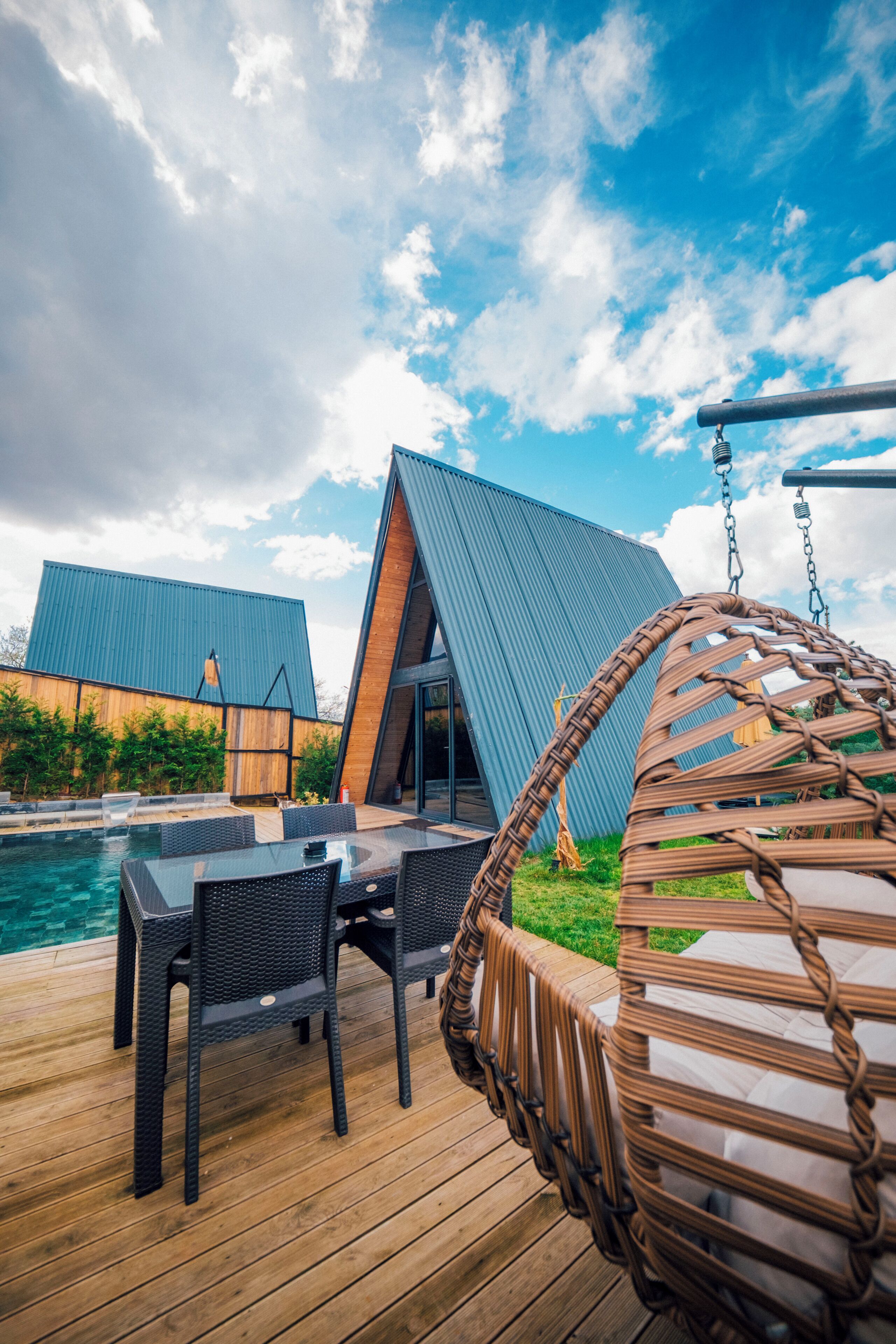 Een houten terras met buitenmeubilair, een hangstoel en een zwembad.