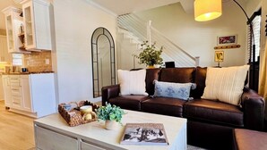 A living room with a brown leather sofa, a white coffee table, and a staircase in the background. -     Freshly Remodeled Oxford Retreat 1 Mile to Ole Miss & The Square (Oxford)