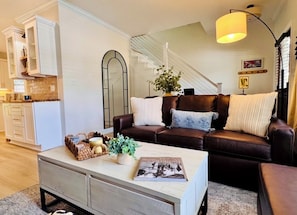 Un salon avec un canapé en cuir marron, une table basse blanche et un escalier en arrière-plan.