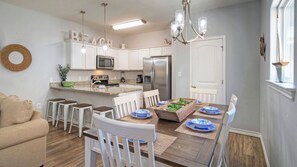 A modern kitchen with white cabinets, a stainless steel refrigerator, and a dining area with a wooden table and white chairs.