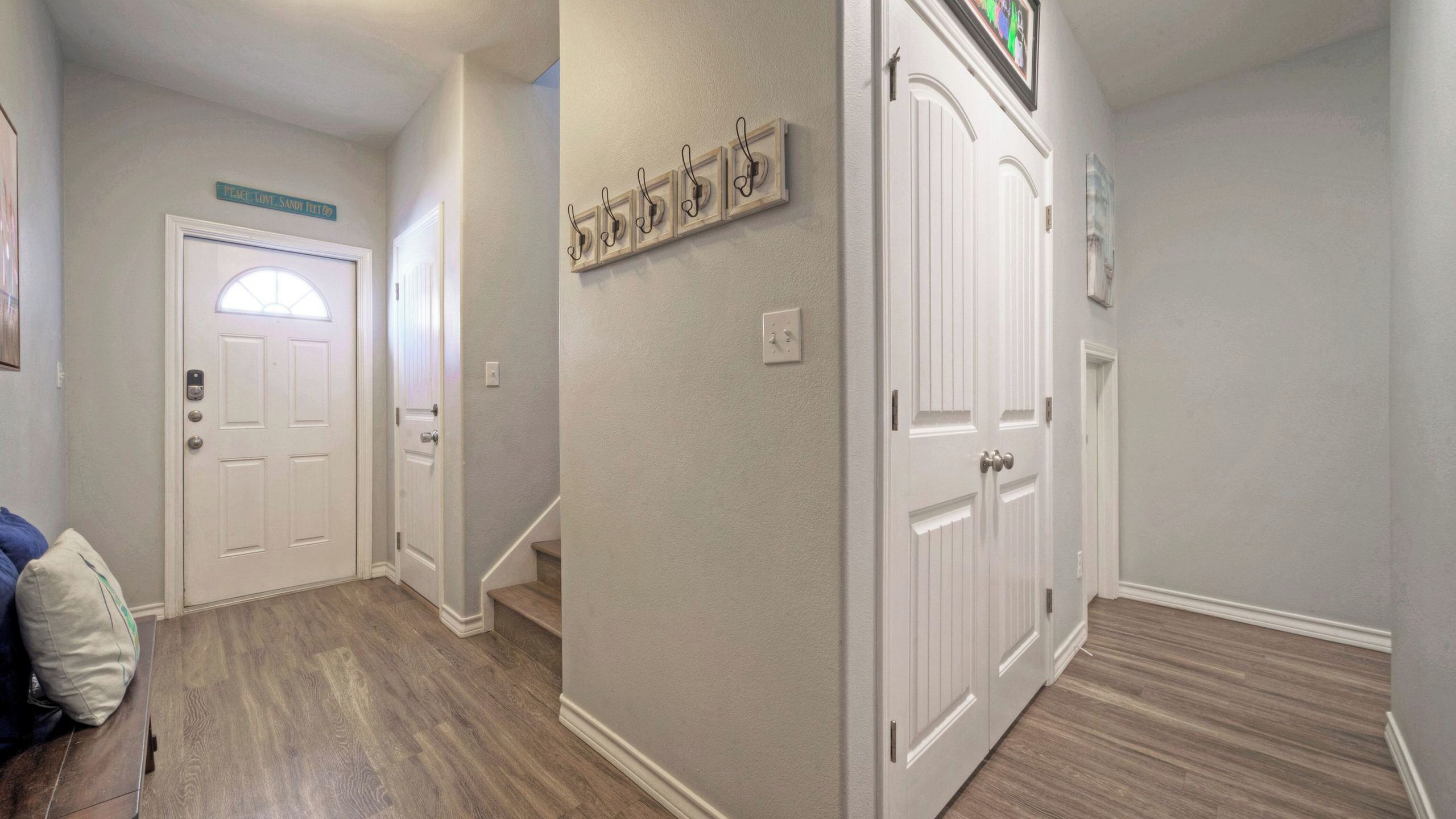 Un pasillo con piso de madera, puertas blancas y un interruptor de luz en la pared.