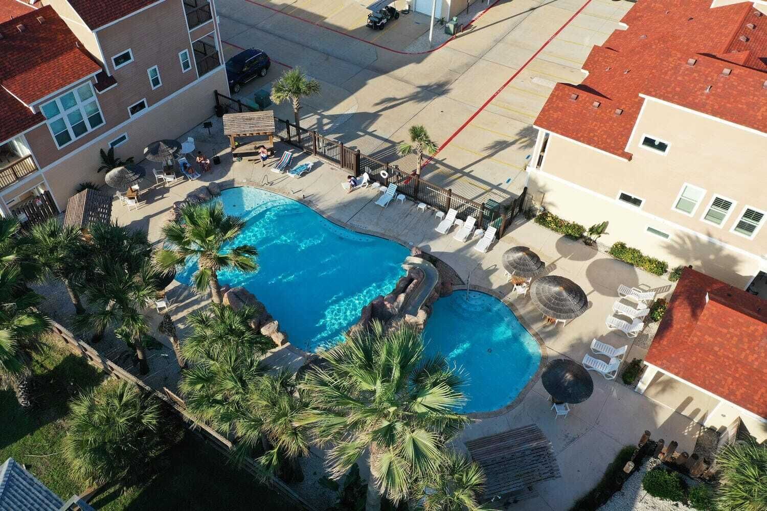 Piscina no terraço com várias áreas, cercada por palmeiras e espreguiçadeiras.