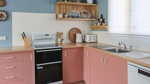 Een keuken met roze kastjes, een zwarte oven, een witte broodrooster en een houten plank met decoratieve objecten.