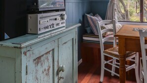 Een kamer met een houten eettafel, witte stoelen, een vintage platenspeler, en een muur versierd met ingelijste foto's.