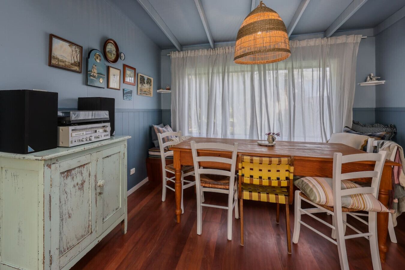 A dining area with a wooden table and chairs, a vintage radio, and a large woven light fixture.