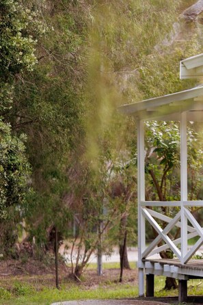 A gazebo with a simple, open structure, surrounded by dense greenery and trees.