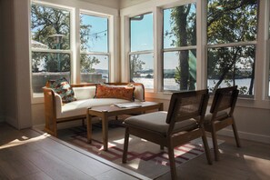 A sunlit room with a sofa, two chairs, and a table, large windows offering a view of a body of water and trees. - Waterfront Retreat - Private Dock & Hot tub (Monkey Island)