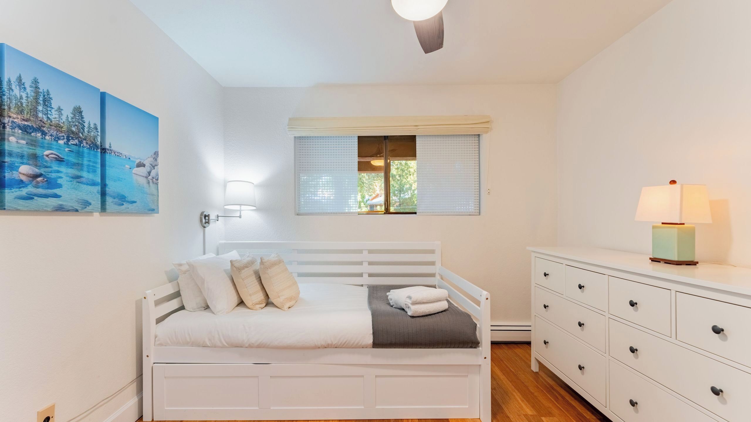 Un dormitorio con cama, lámpara de noche, cómoda y ventana con persianas.