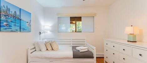 Un dormitorio con cama, lámpara de noche, cómoda y ventana con persianas.
