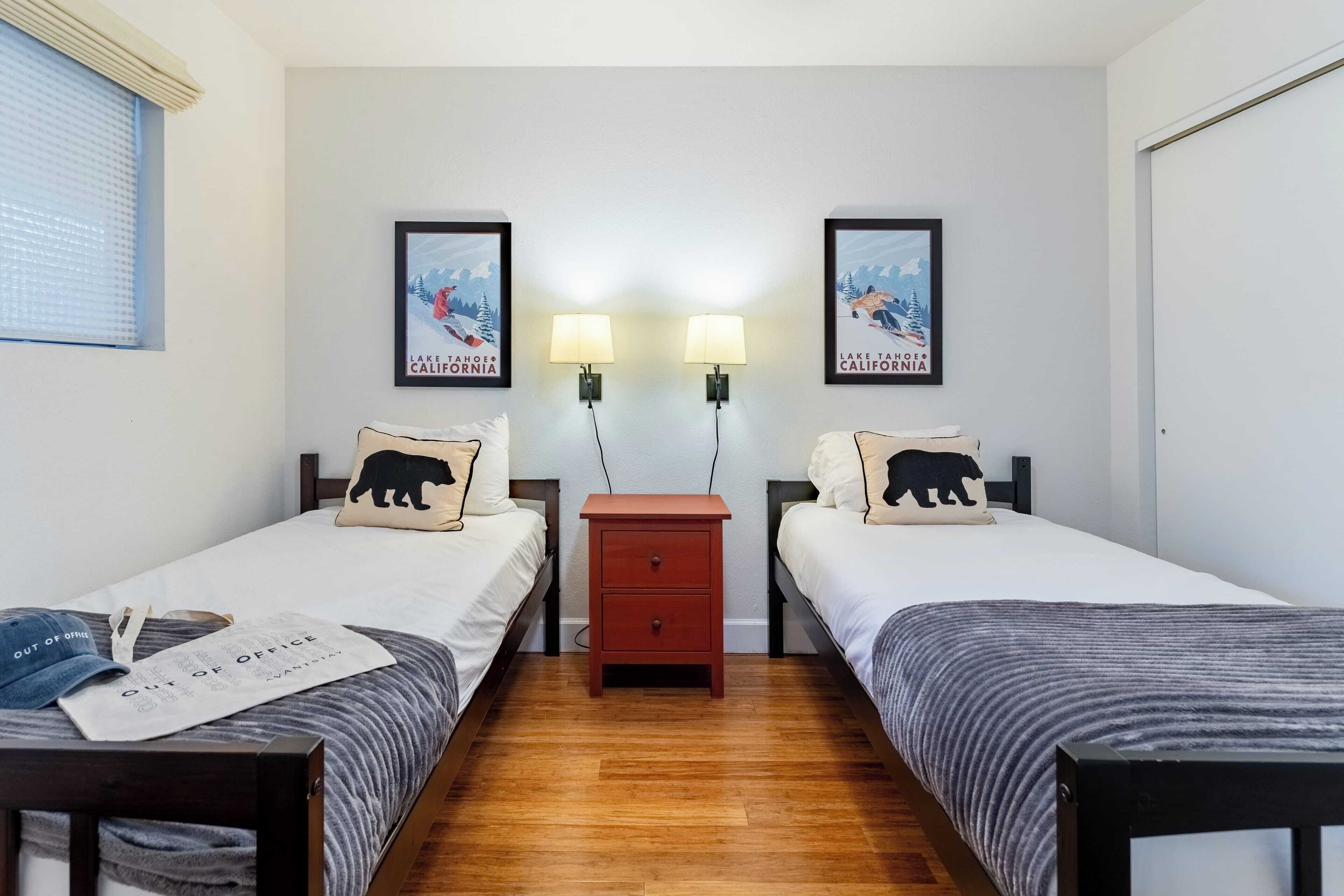 A twin room with two beds, a nightstand, two wall-mounted lamps, and two framed posters of Lake Tahoe, California.