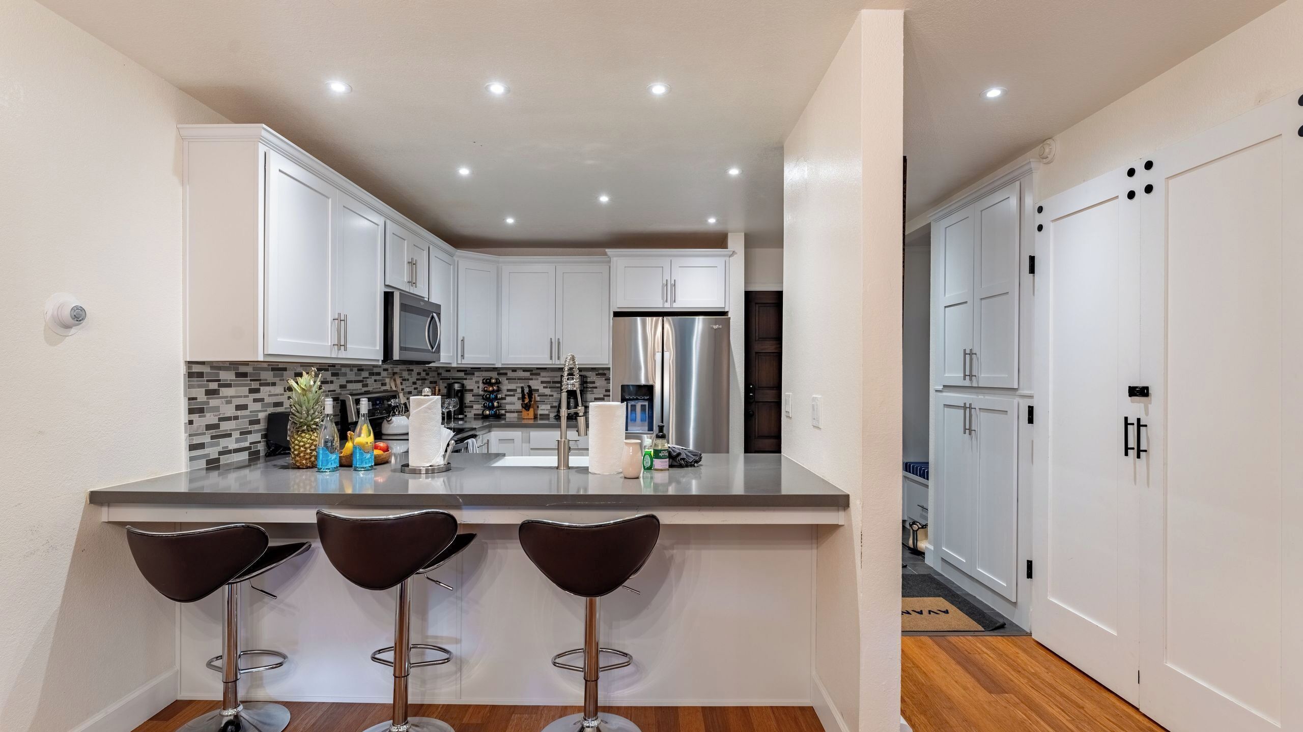 A modern kitchen with white cabinets, stainless steel appliances, and a bar area with stools.