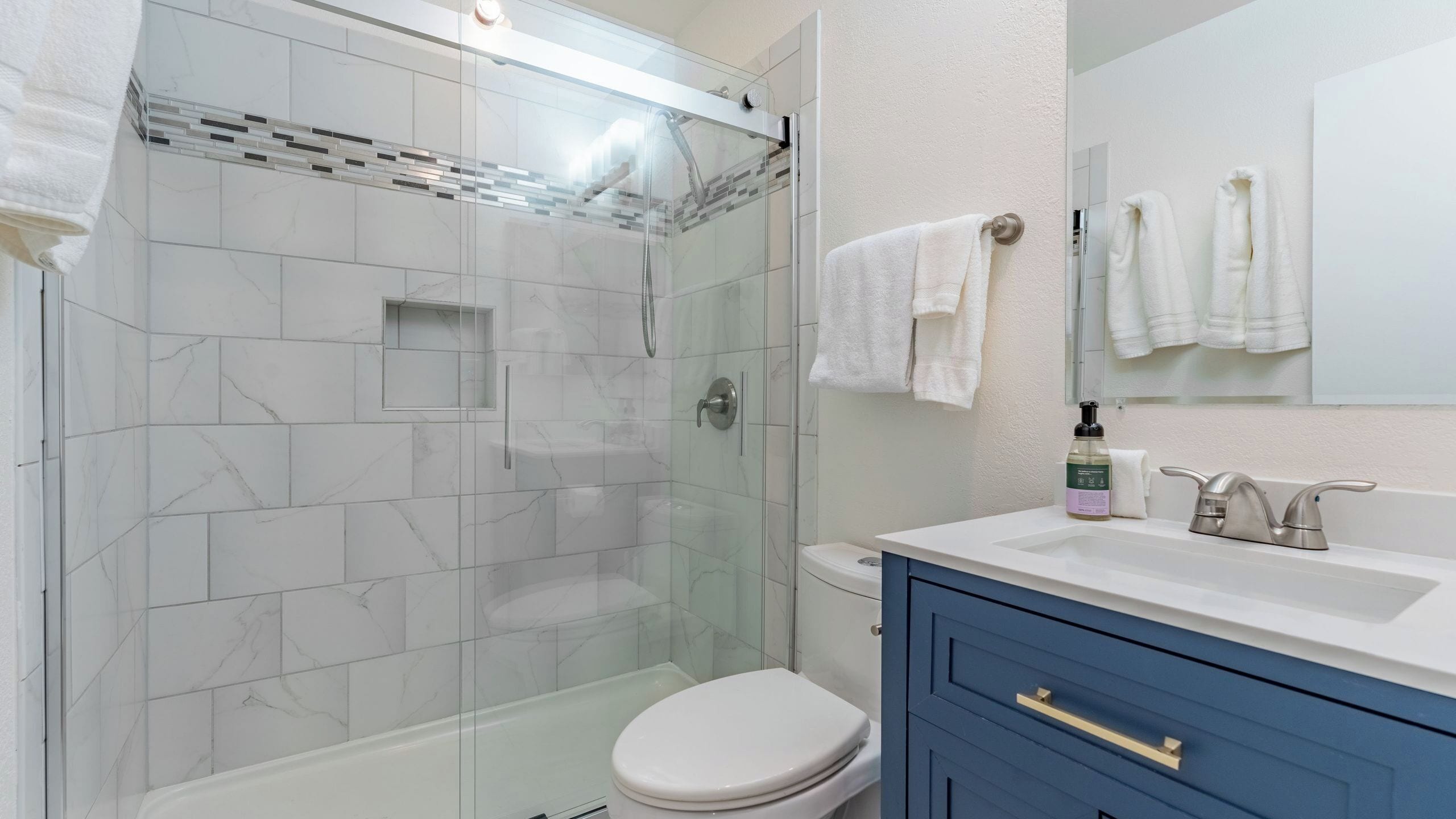 A modern bathroom with a glass-enclosed shower, a white toilet, a sink with a mirror, and blue cabinets.