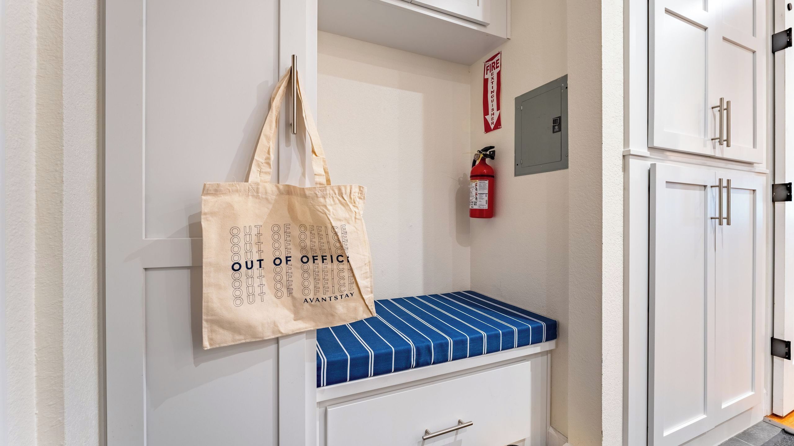 A hallway with a white bench, a fire extinguisher, and a fire exit sign.