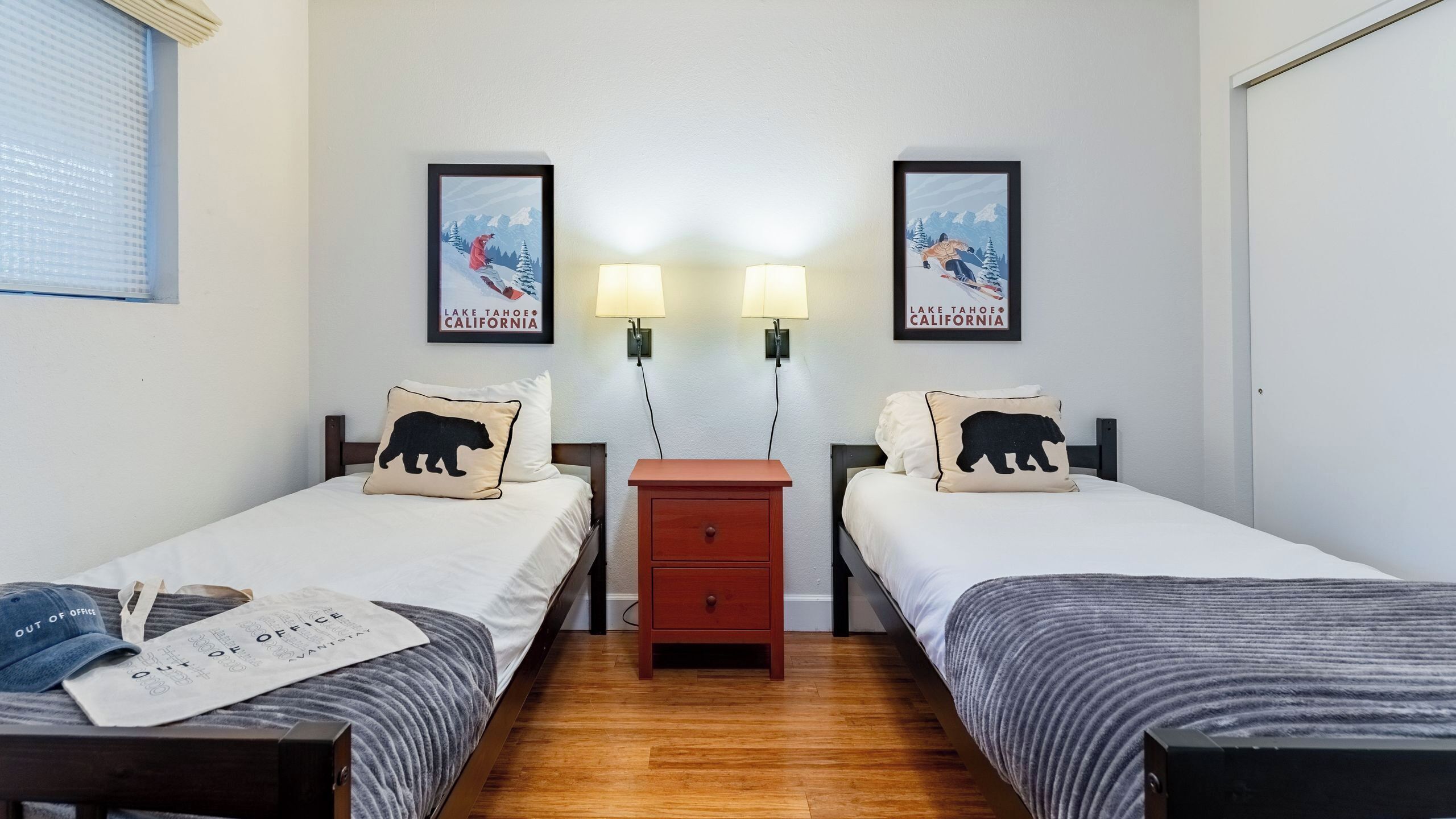 Quarto de hotel com duas camas, uma mesa de cabeceira e luminárias fixadas na parede.