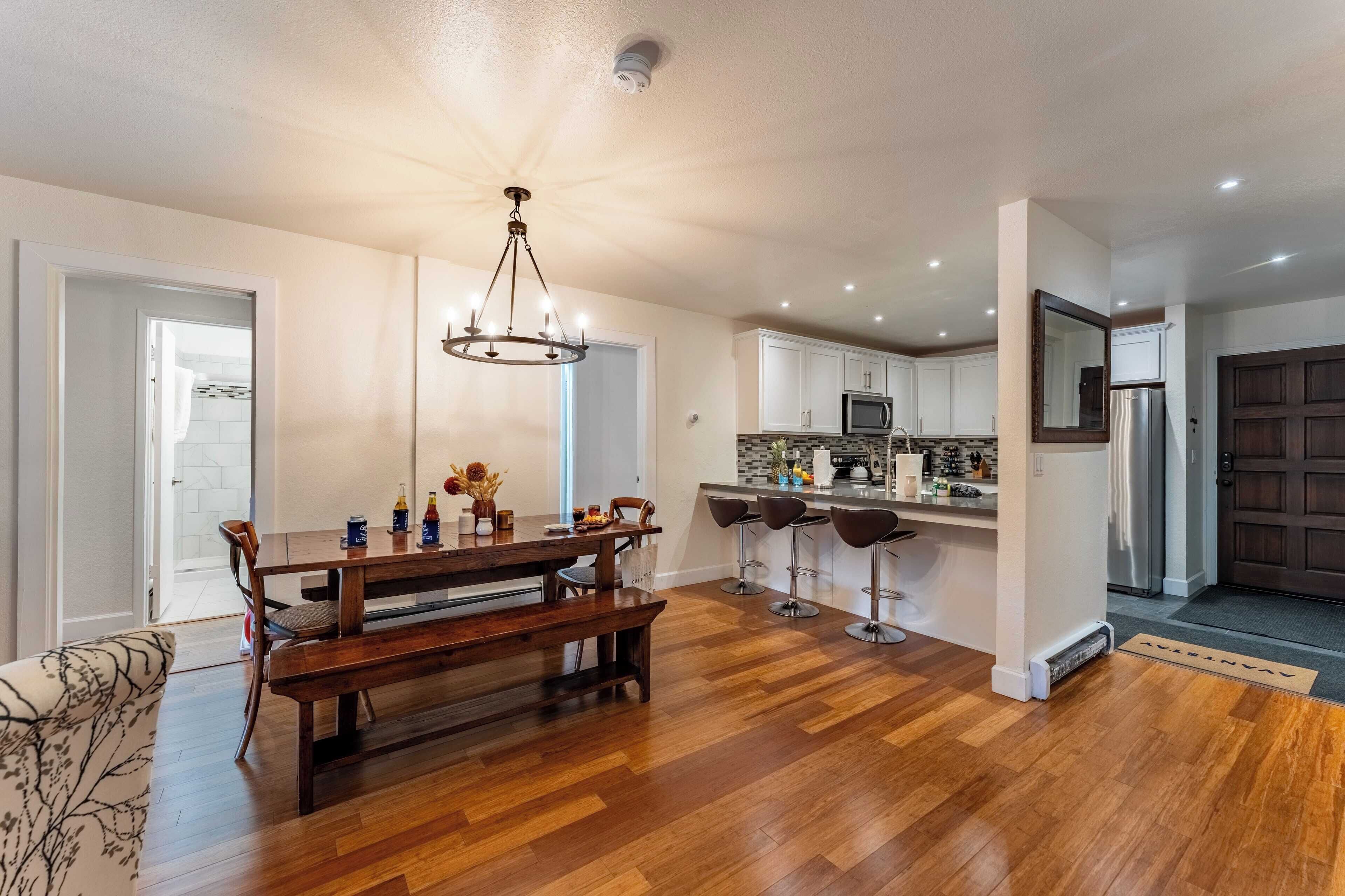 Une cuisine moderne avec un plancher en bois, un îlot central, des tabourets de bar et un lustre.
