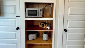 Une petite cuisine équipée d’un four à micro-ondes, d’une machine à café et d’un haut-parleur posé sur une étagère, avec un tableau encadré au-dessus.
