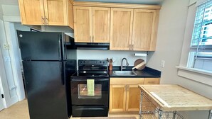 Une cuisine de taille réduite, avec des meubles de rangement en bois, un réfrigérateur noir, une cuisinière et un évier.