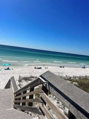 A wooden staircase leading to a beach with clear blue water and white sand.