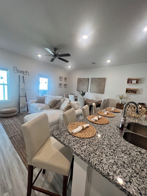 A modern kitchen with granite countertops, a central island with bar stools, and a dining area with a high table and chairs.