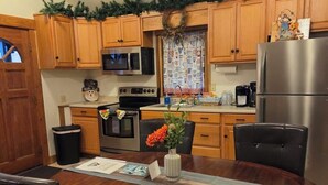 A kitchen with wooden cabinets, a stainless steel refrigerator, a microwave, and a stove. There is a dining table with chairs and a vase with flowers.