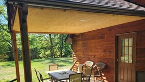 A covered patio with a table and chairs, a wooden door, and a view of a grassy yard.