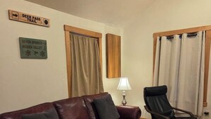 A living room with a leather sofa, a glass coffee table, a lamp, and two signs on the wall.