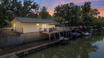 A house with a dock extending into a calm body of water, surrounded by trees.