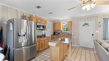 A compact kitchen with a stainless steel refrigerator, wooden cabinets, a small island, and a ceiling fan.