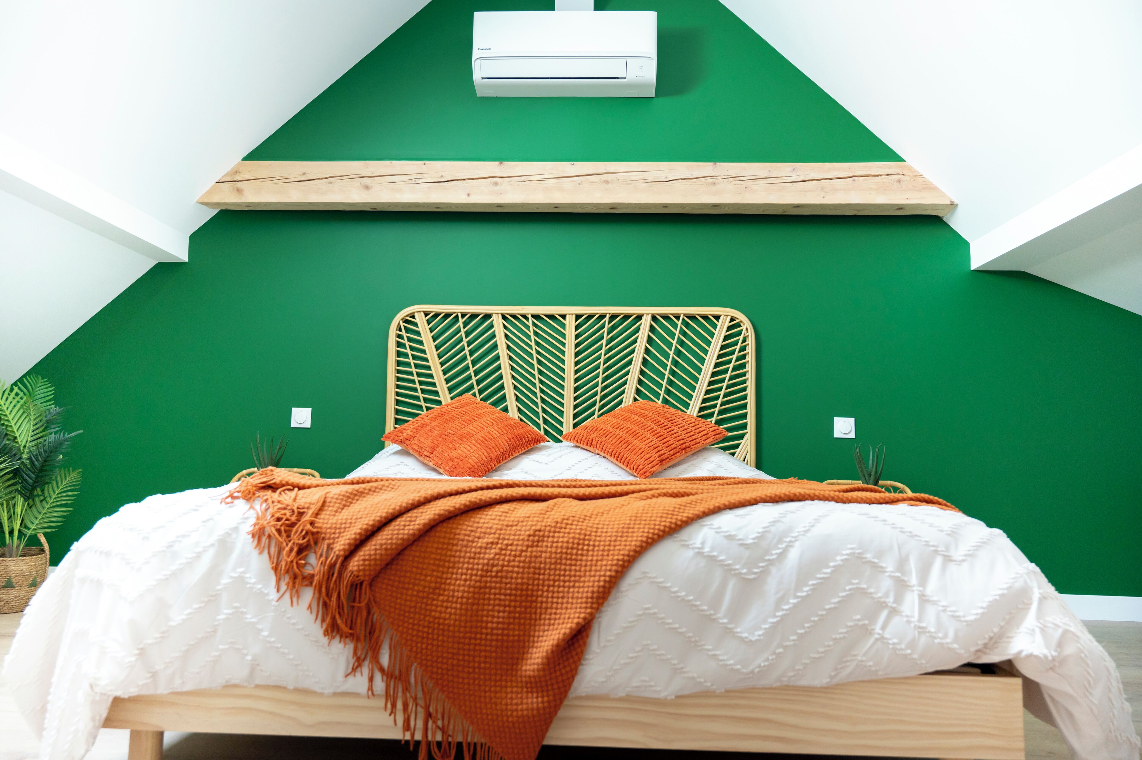 Ein Bett mit Holz-Kopfteil, weißer Bettwäsche und einer orangefarbenen Tagesdecke.