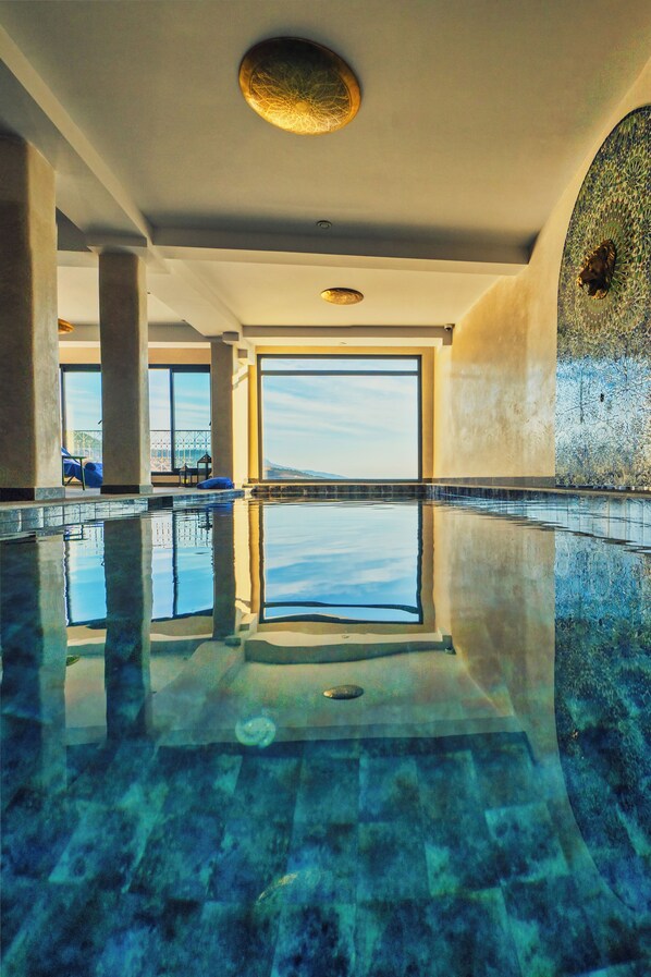 An indoor swimming pool with clear water, large windows, and a view of the landscape.