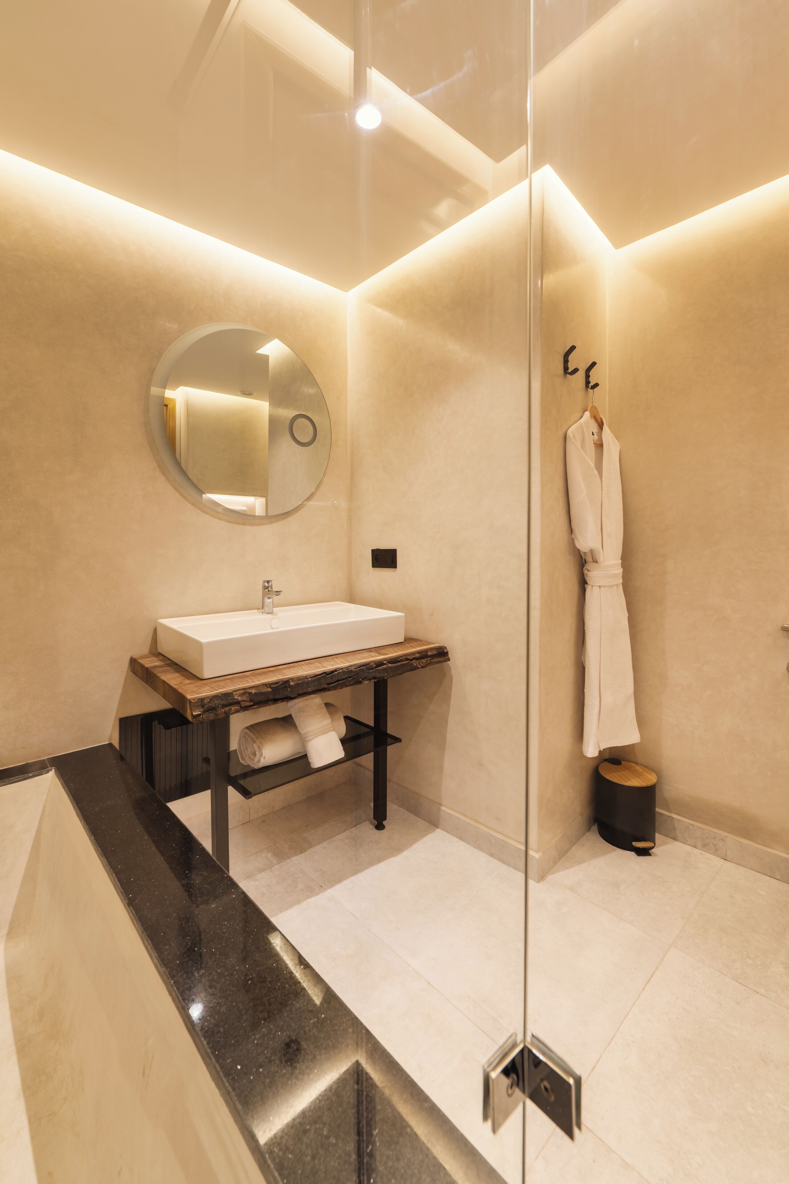 A modern bathroom with a rectangular sink, a round mirror, and a robe hanging on a rack.