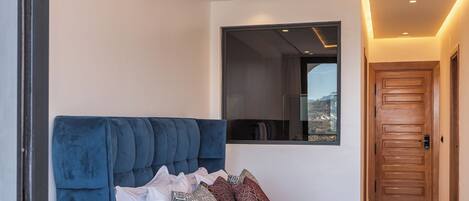 A modern bedroom with a blue headboard, a large bed with patterned bedding, a bedside table with a decorative vase, and a ceiling with intricate geometric patterns.