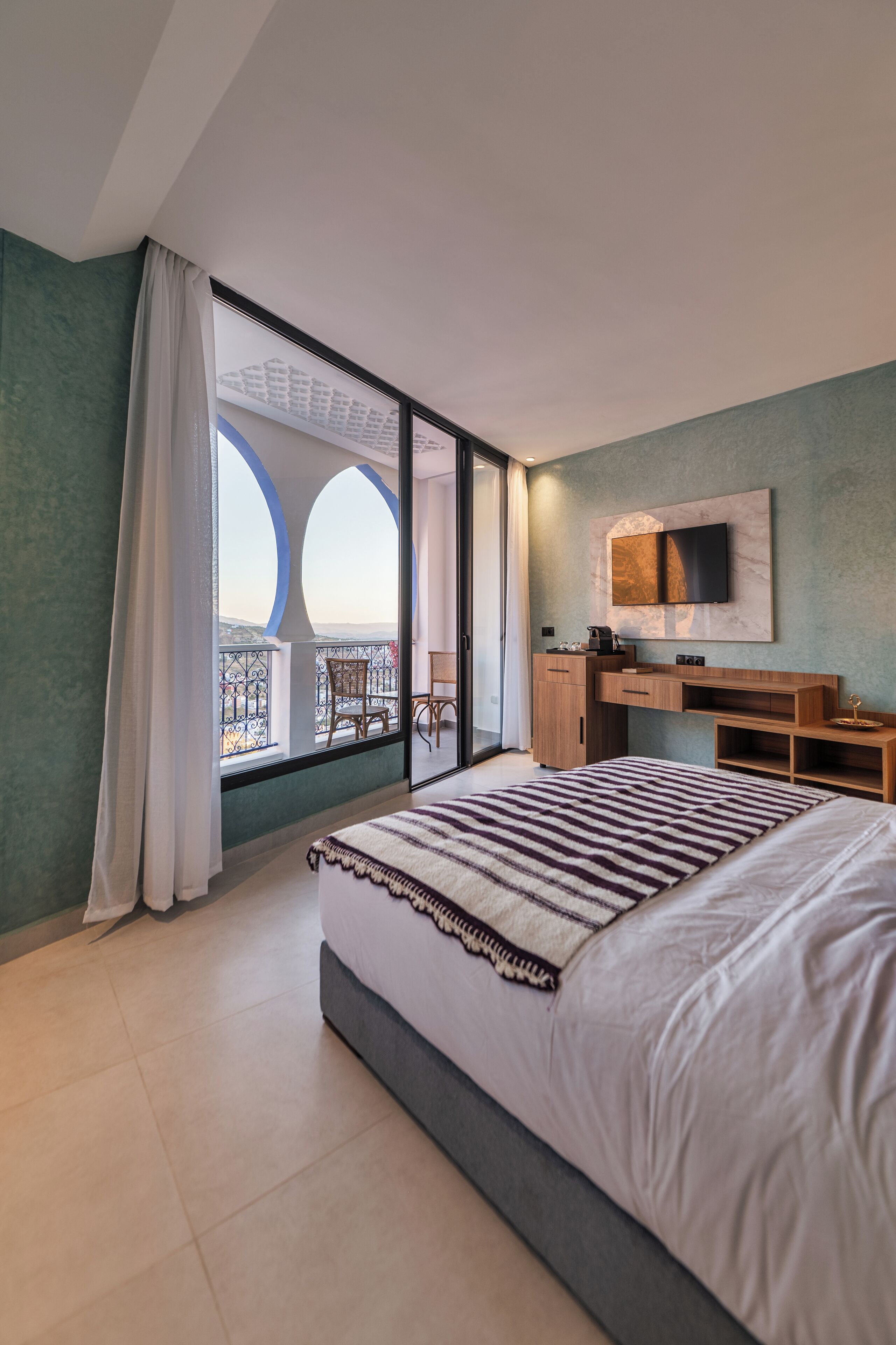 Un dormitorio moderno con una cama grande, un escritorio, un televisor y un balcón con vistas.