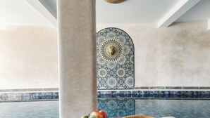 Una habitación con un gran pilar, un muro decorativo, una mesa con una cámara, manzanas y un sombrero.