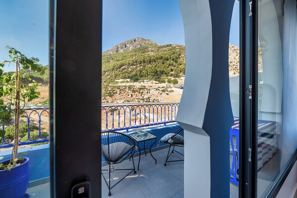 Un balcón con vistas a un paisaje montañoso, una mesa con sillas y una planta en maceta.