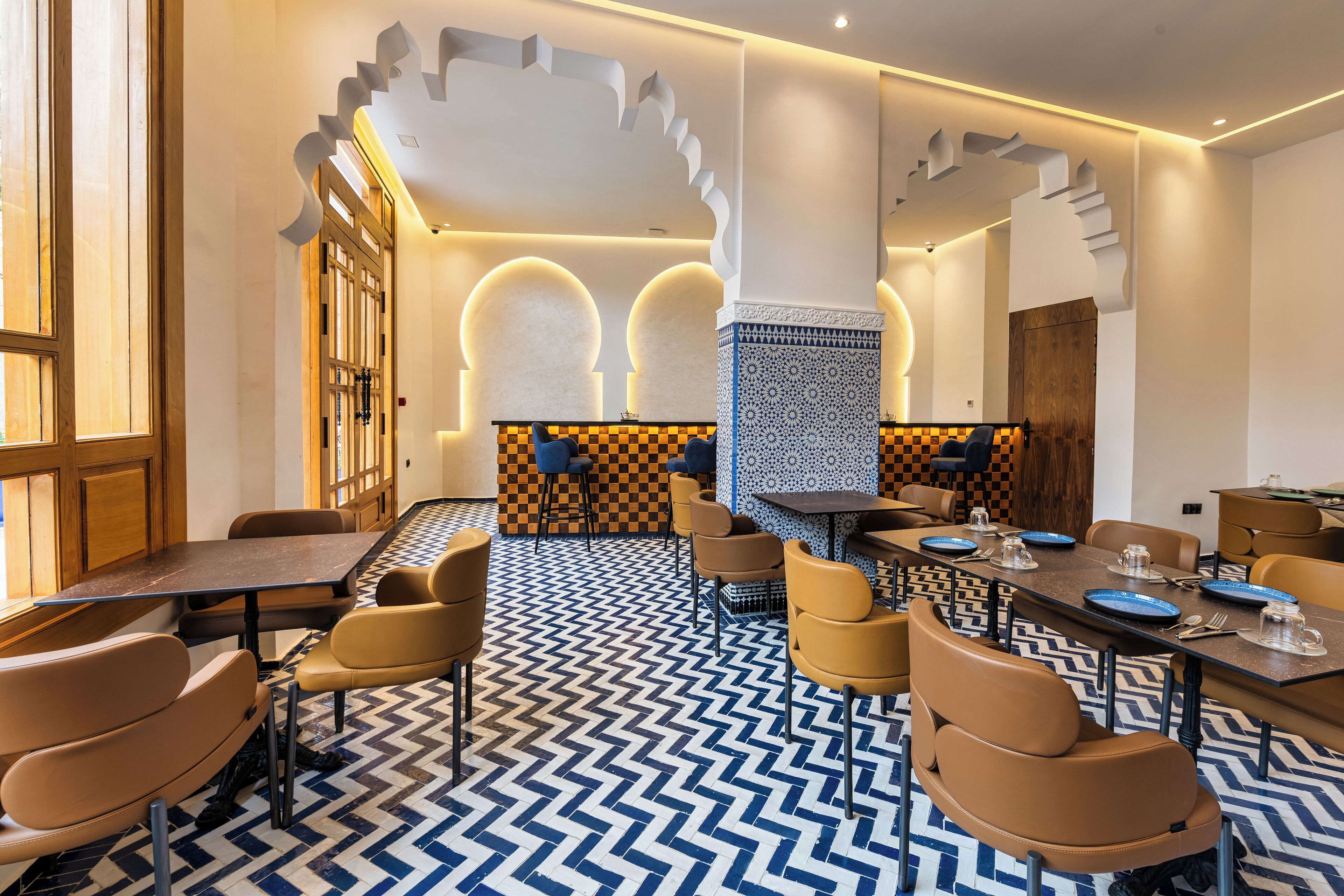 A modern dining area with a checkered floor, wooden furniture, and a central column with a patterned design.